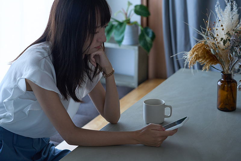 暗い表情でスマートフォンを見つめる女性