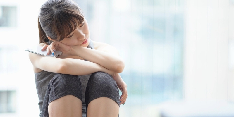 膝を抱えて悩む、スポーツウェア姿の女性の写真