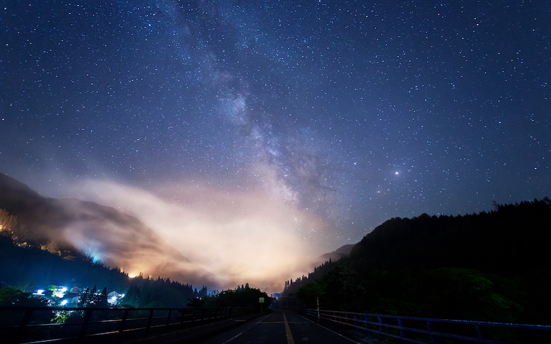 山あいを包む霧の上に天の川が輝く空の写真