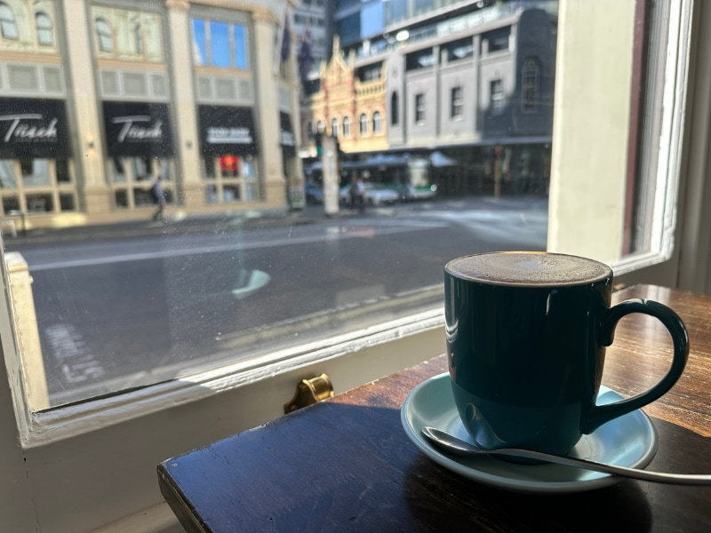 ブルーのコーヒーカップと窓から見える街の写真