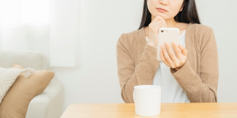 スマホを見て考える女性の写真