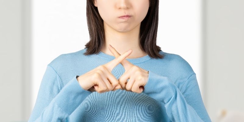 頬を膨らませ、不満そうな表情の女性。指でバッテンを作っている