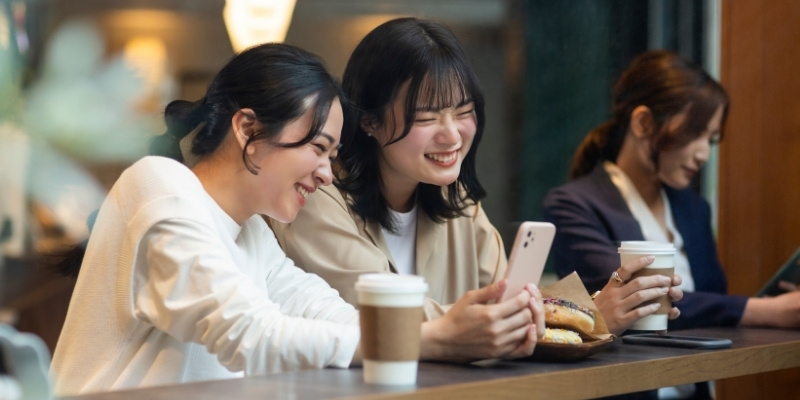 カフェでスマホを見て笑っている女性二人の写真