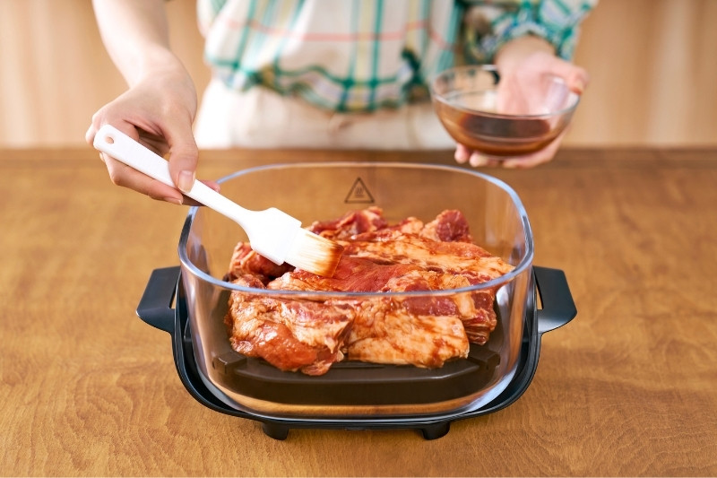 ガラスコンテナでチキングリルにソースを塗って下ごしらえしている写真