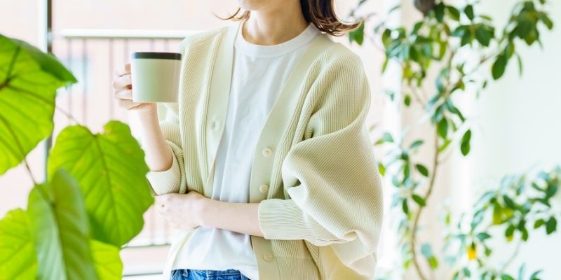 緑に囲まれた部屋でマグカップを片手に持っている女性の写真