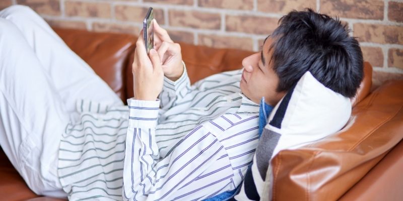 ソファに寝転がってスマホを操作する男性の写真
