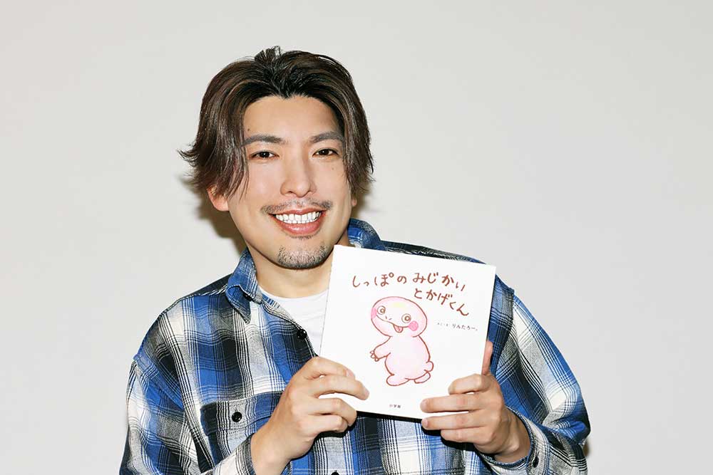 絵本『しっぽのみじかいとかげくん』を手に持つりんたろー。さん