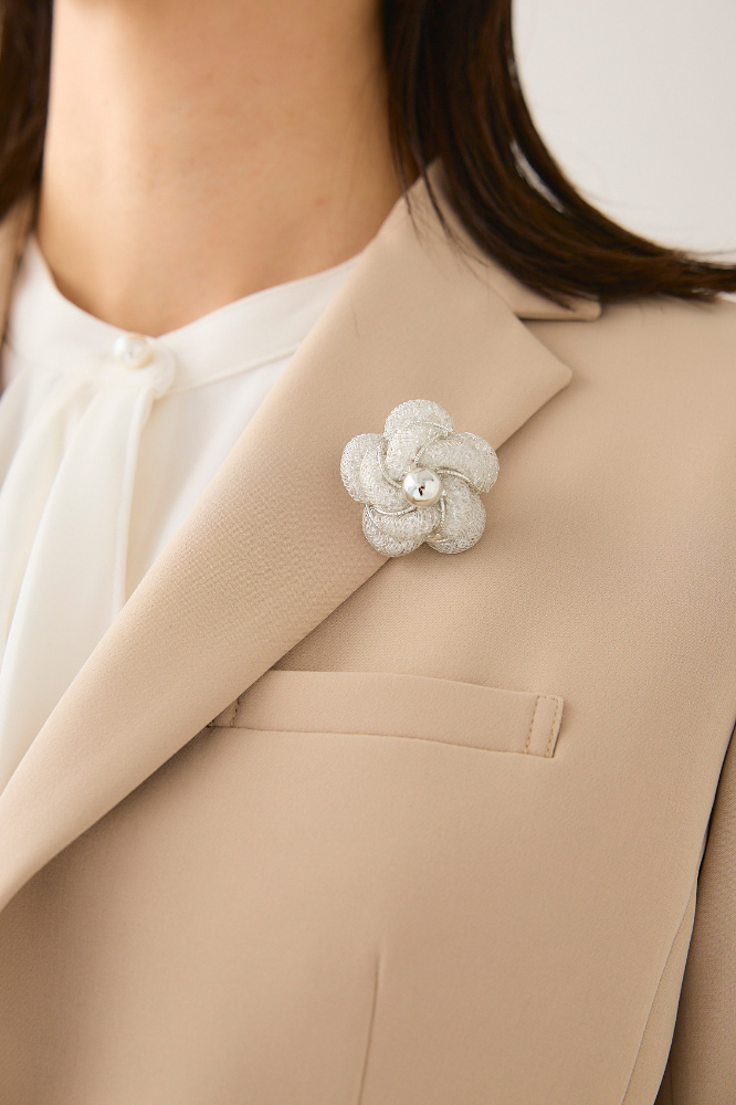 ベージュのジャケットにフラワーコサージュをつけた人の寄り写真