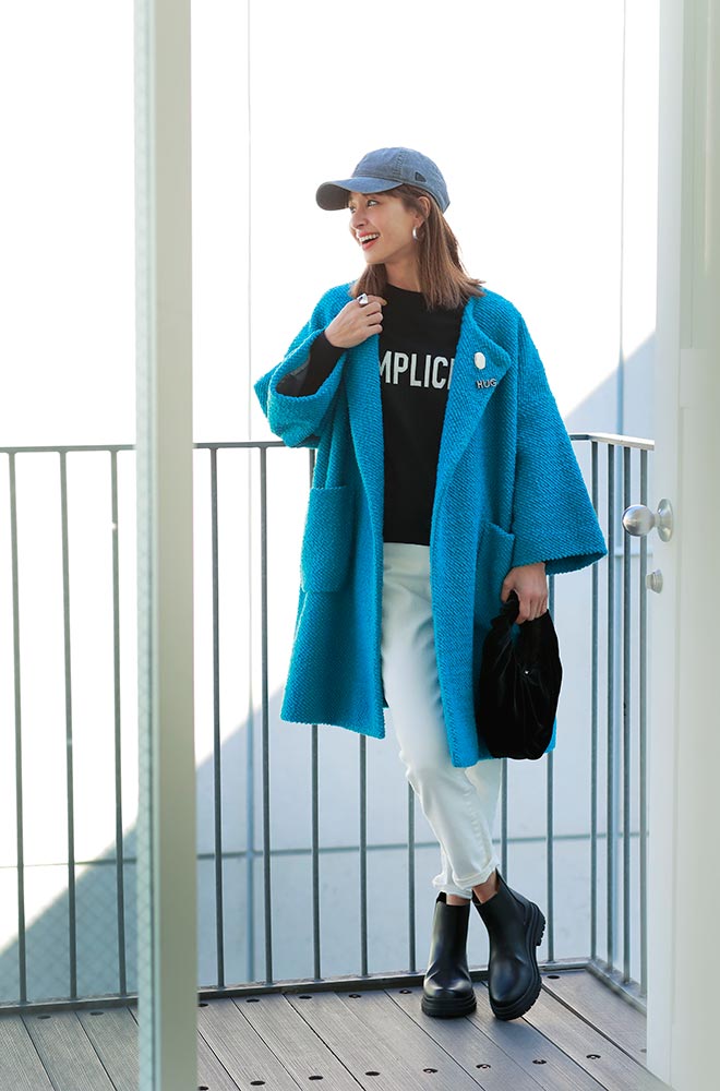 黒地のロゴニットと白デニムにブルーのミドル丈コートをはおったモデル写真