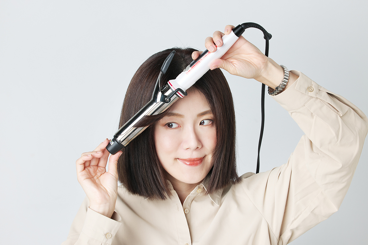 前髪なしボブヘアのモデルが、サイドの髪をアイロンで外巻きにしている写真