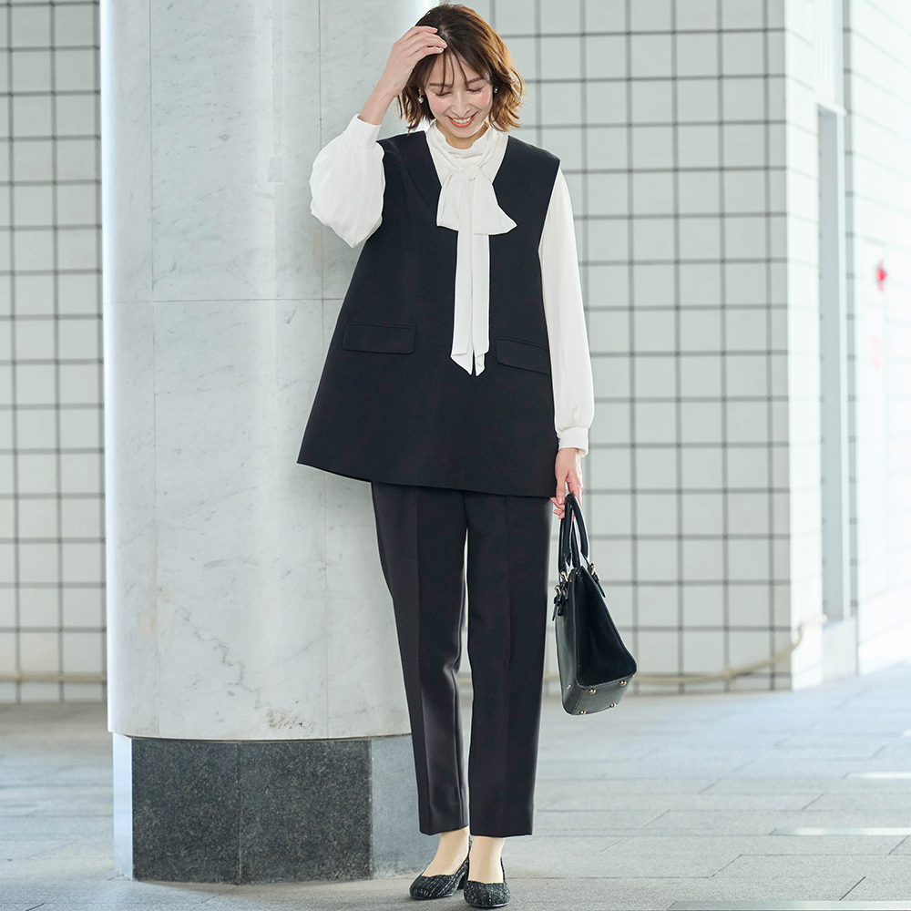 ネイビーのベスト、パンツ、白のボウタイブラウスを着用したモデル。