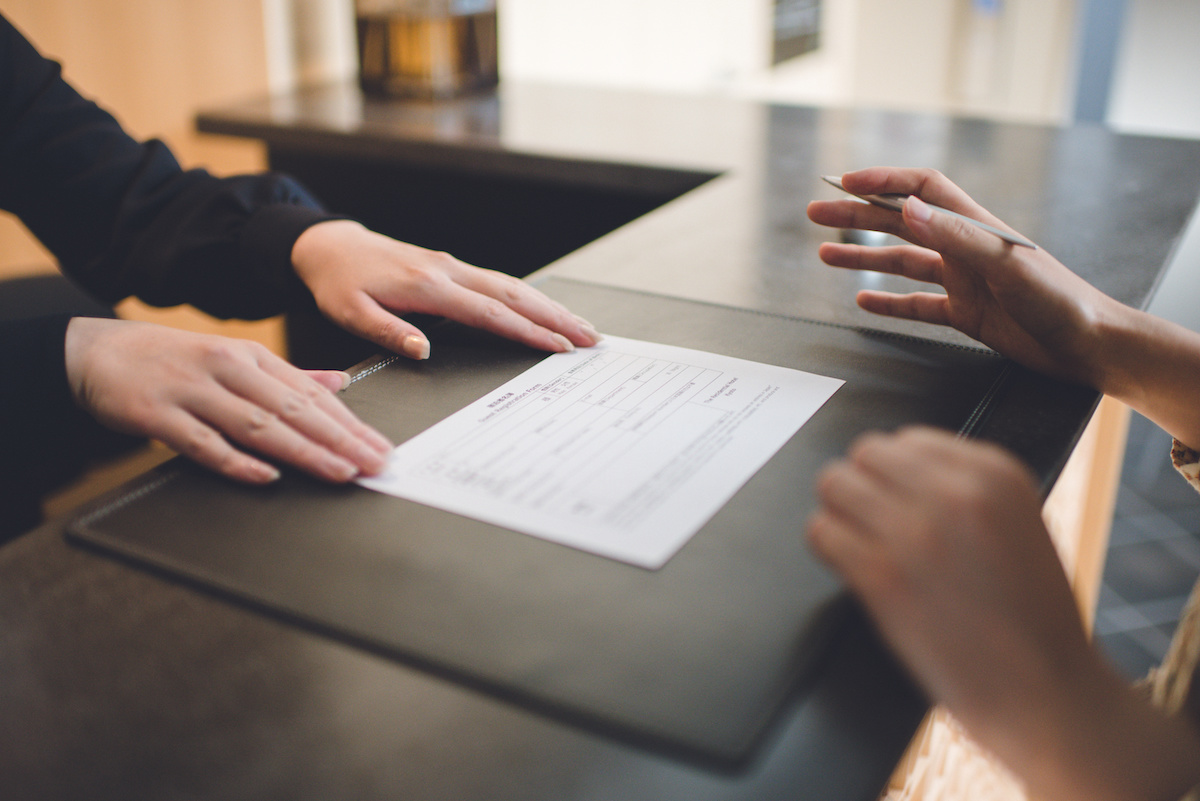 ホテルのフロントで紙にペンで記入しようとする人の手元の写真