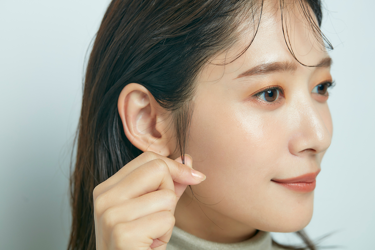 こめかみの髪を親指と人差し指でつまんでヘアワックスをつけている写真