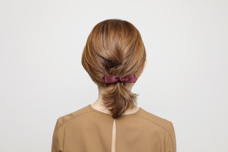 ふっくらとしたひとつ結びにえんじ色のリボンの形のヘアアクセをあしらった写真　後頭部