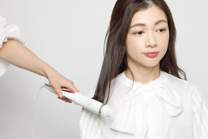ヘアアイロンで毛先を巻いているロングヘアの写真