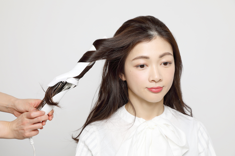 ロングヘアの表面の髪をアイロンで巻いている写真