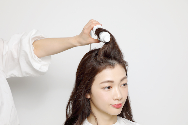 ロングヘアのトップの毛束をアイロンで巻いている写真