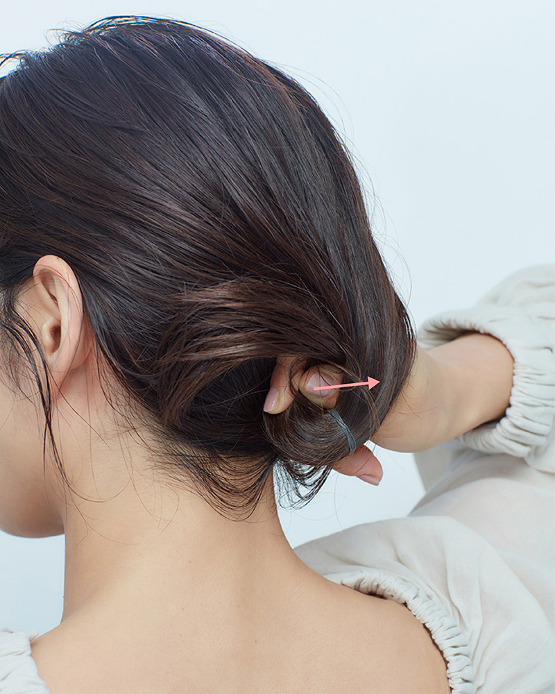 結び目の上に人差し指を入れてつくった穴に、毛束を左から入れている後頭部写真