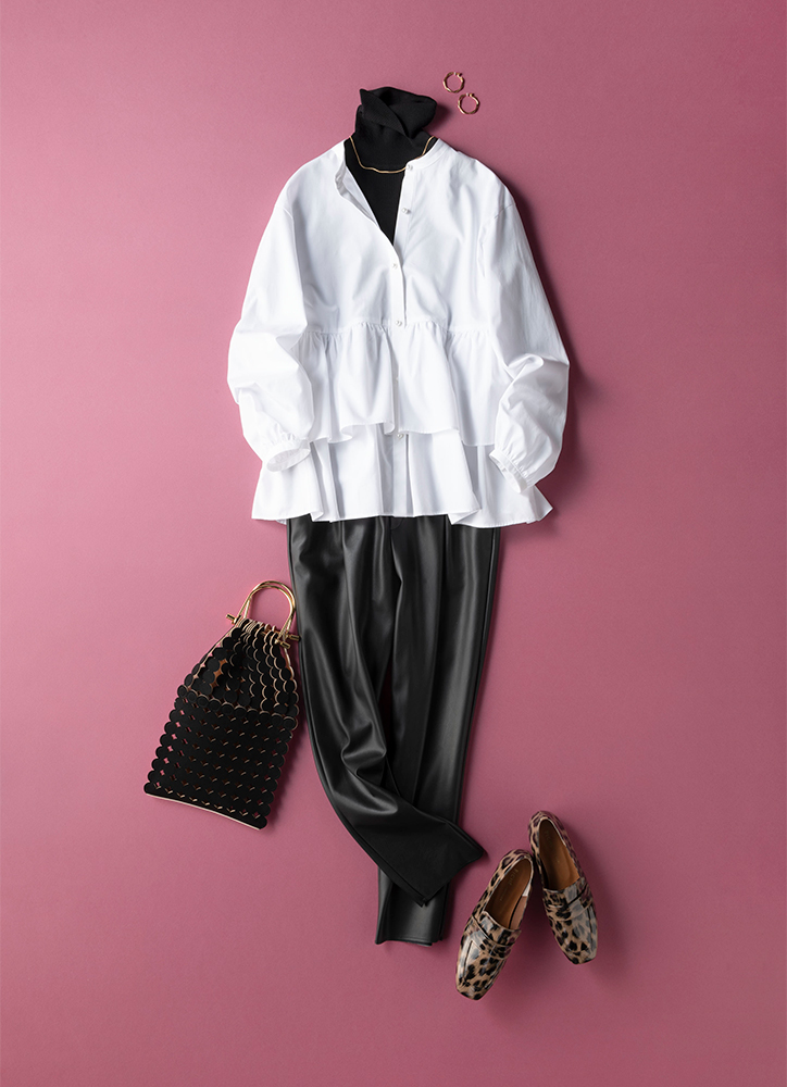 白のペプラムデザインのブラウスの下に黒のタートルニットを重ね着し、黒のエコレザーパンツをはいたコーデ