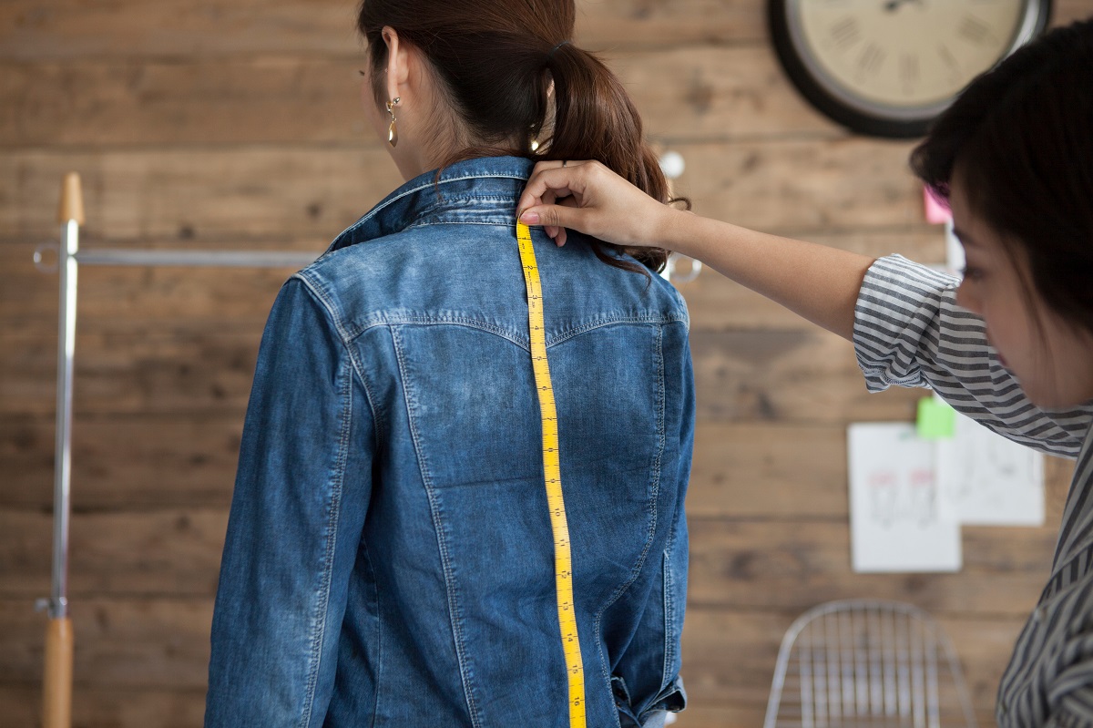 黄色いメジャーで背面のサイズを計測している人、計測されている人の写真