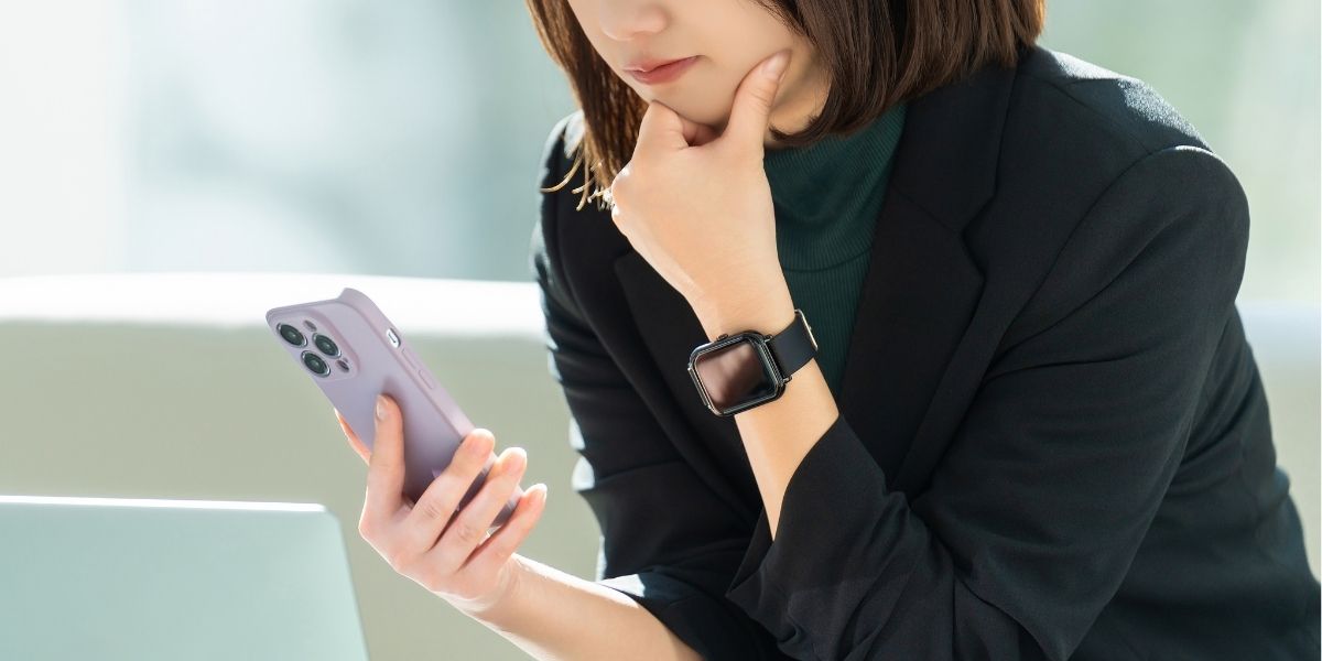 スマホを見ながら考え込む女性の写真