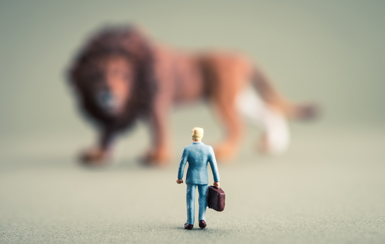 大きなライオンのオブジェの前にビジネスマンの小さなオブジェが置かれており、立ち向かっているさまを表現した写真