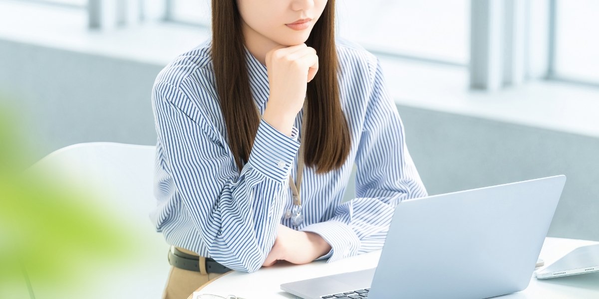 ノートパソコンの前で考える女性の写真