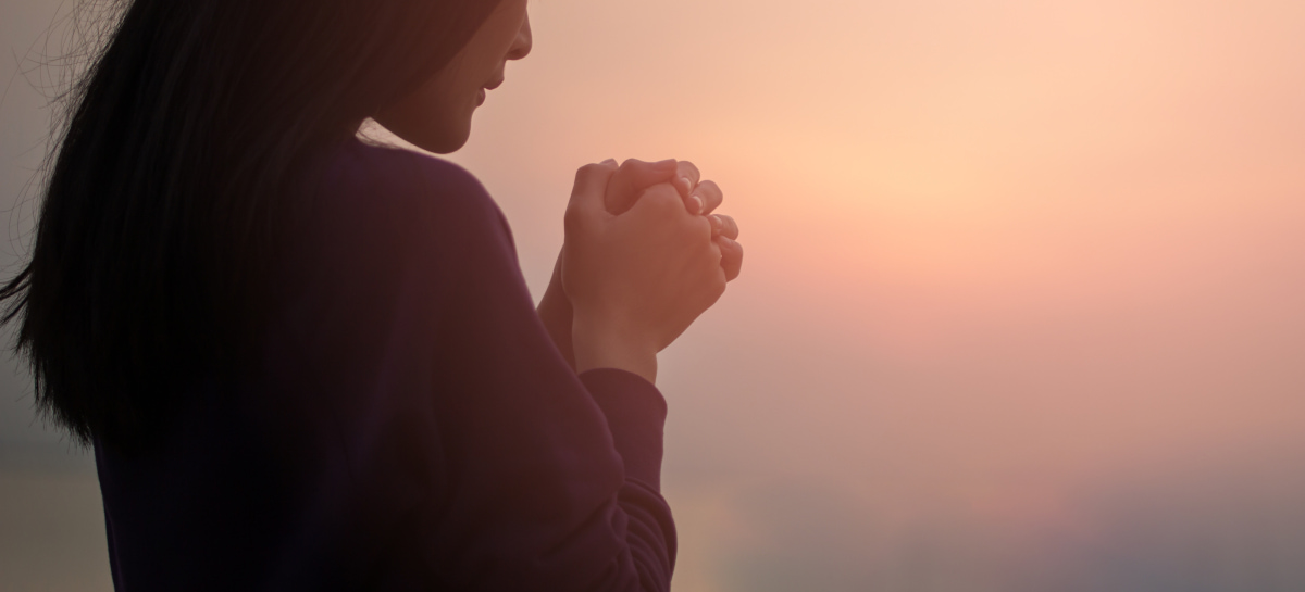 夕暮れに祈る女性の後姿の写真