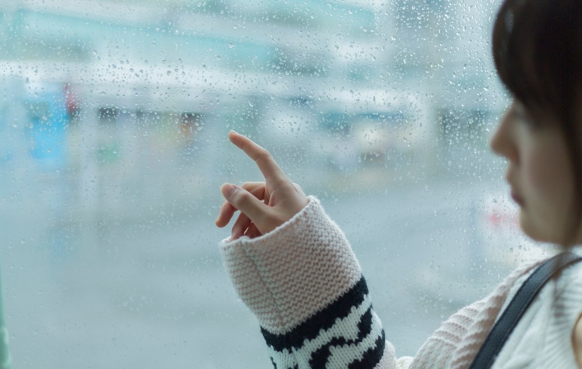 窓の雨を指でなぞる女性の写真