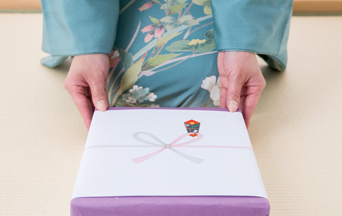 着物を着た女性がのし付きの贈り物を両手で差し出す様子
