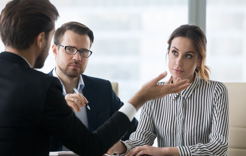 話しているビジネスマンを懐疑的な目で見つめる男女の写真
