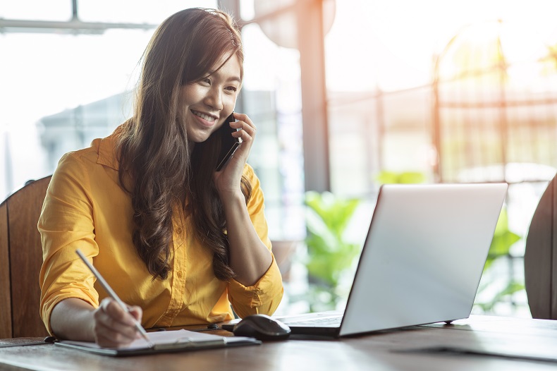 PCと手帳を開いてスマホで電話する女性の写真