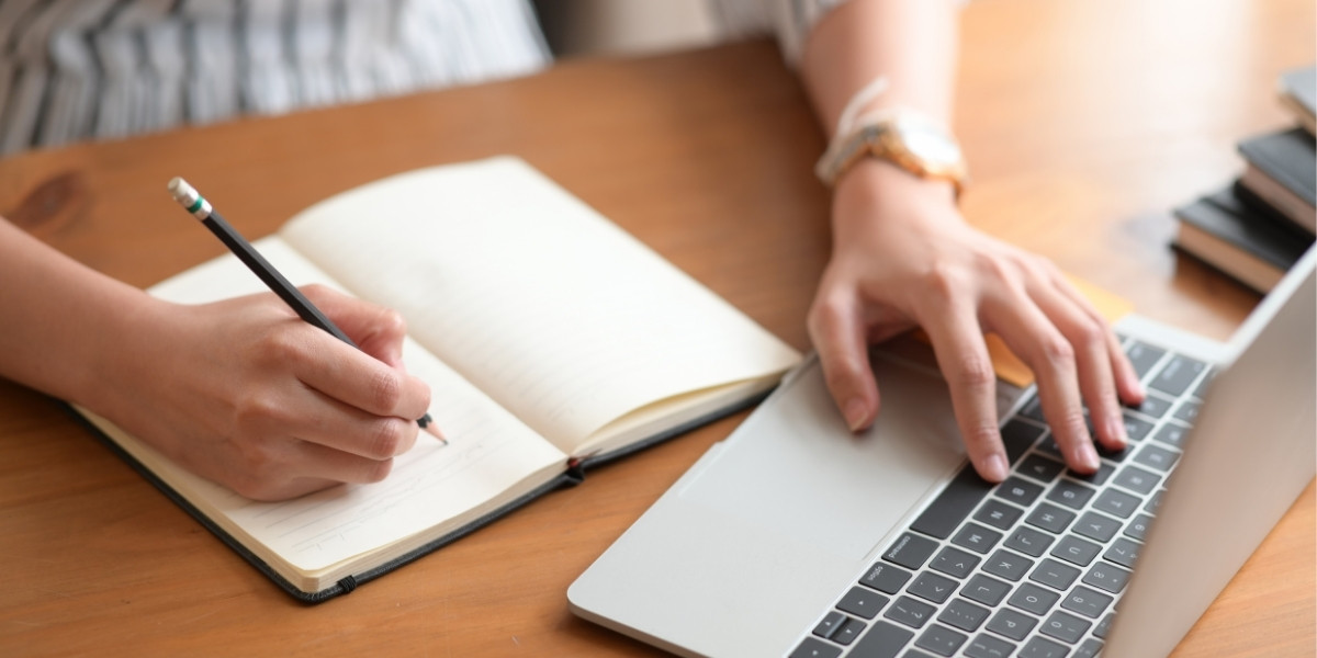 ノートパソコンを見ながら手帳にメモを取る女性の写真