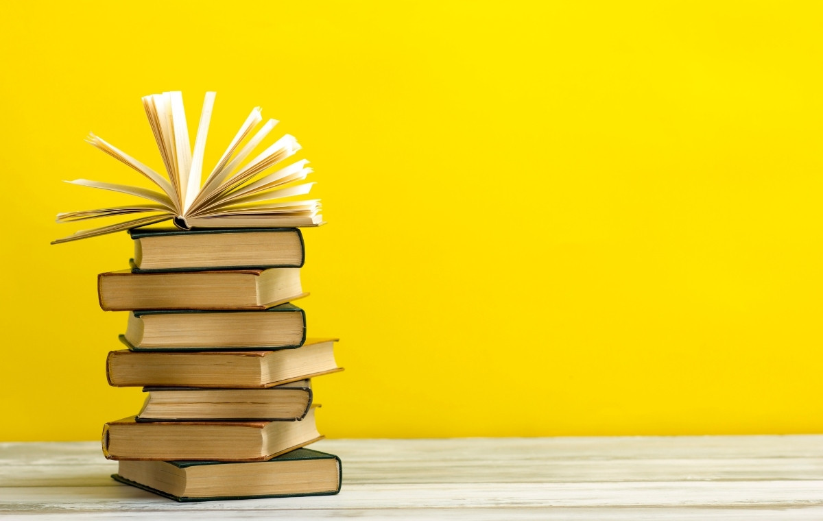 黄色の背景とフローリングに、本が積まれておかれている写真