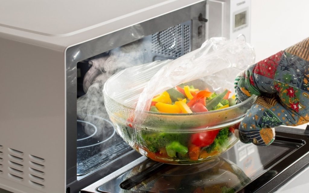 レンジからできあがった蒸し野菜を取り出している写真