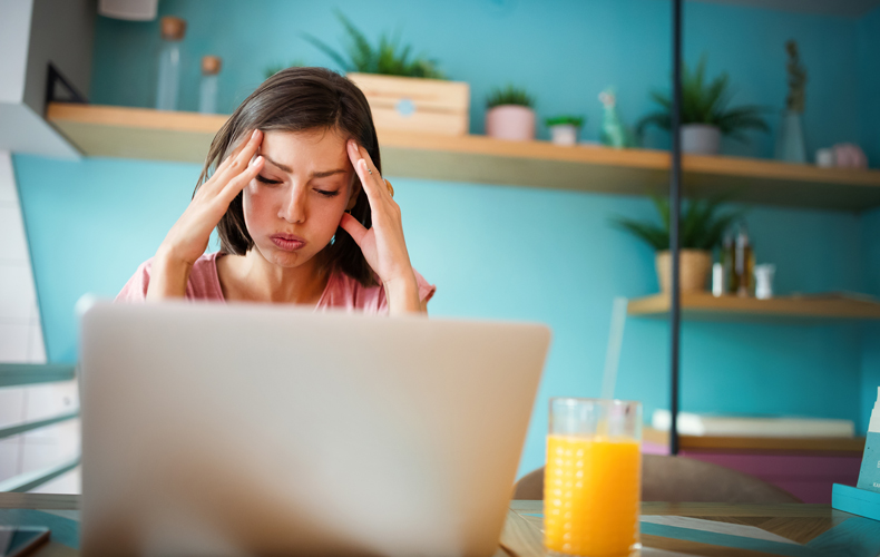 ノートパソコンの前で頭を抱えて悩む女性の写真