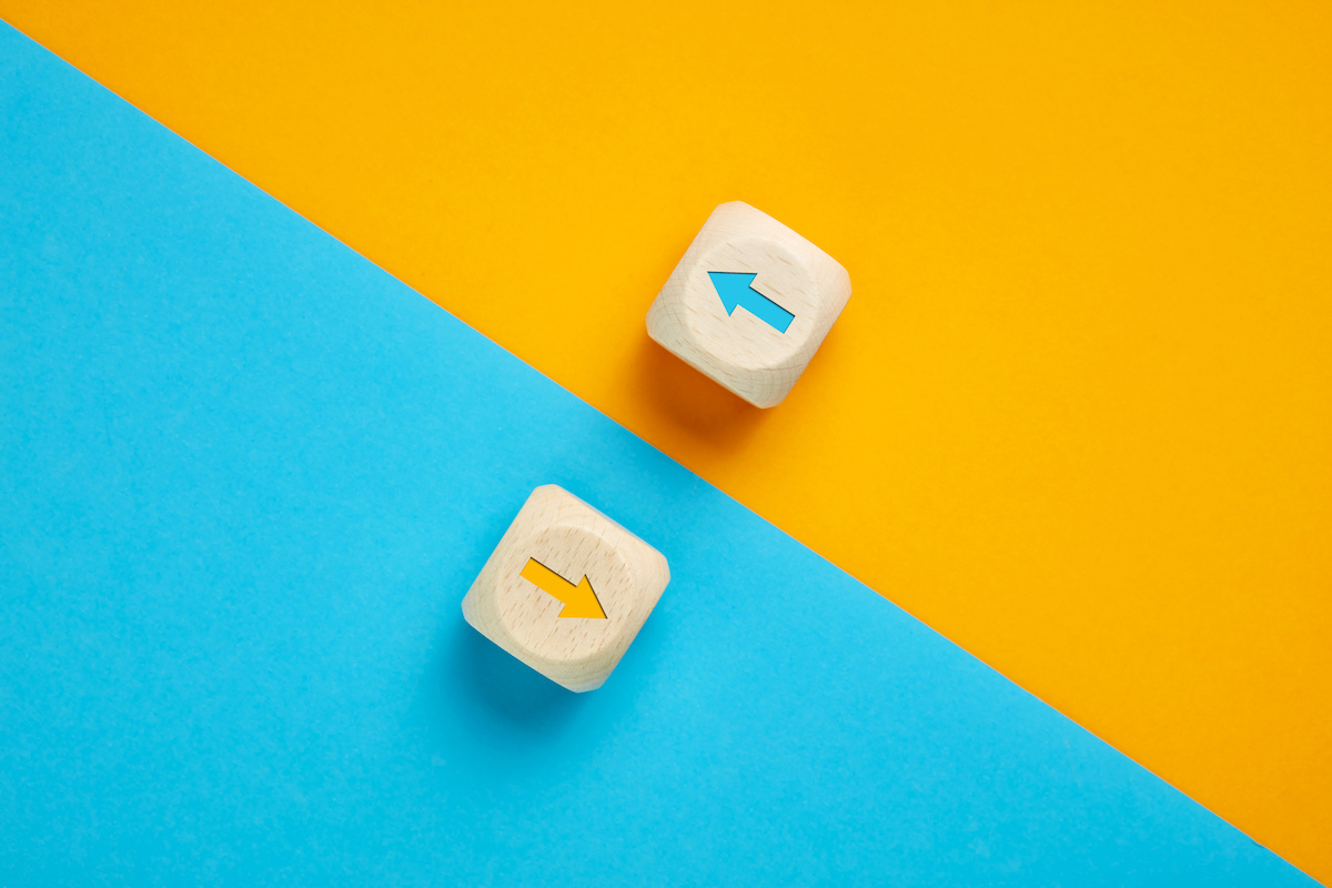 黄色と水色の背景、斜め上と斜め下をさした矢印が描かれた木製ブロック