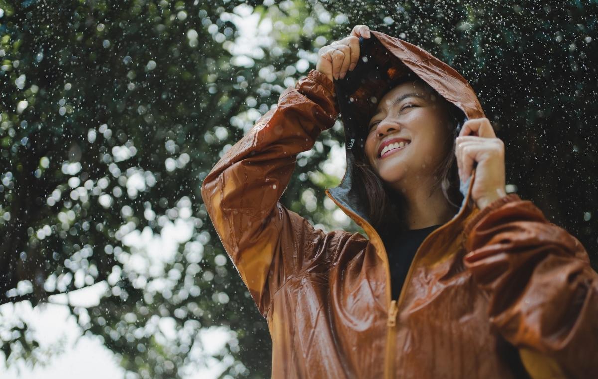 合羽を着て楽しそうに雨を浴びる女性の写真