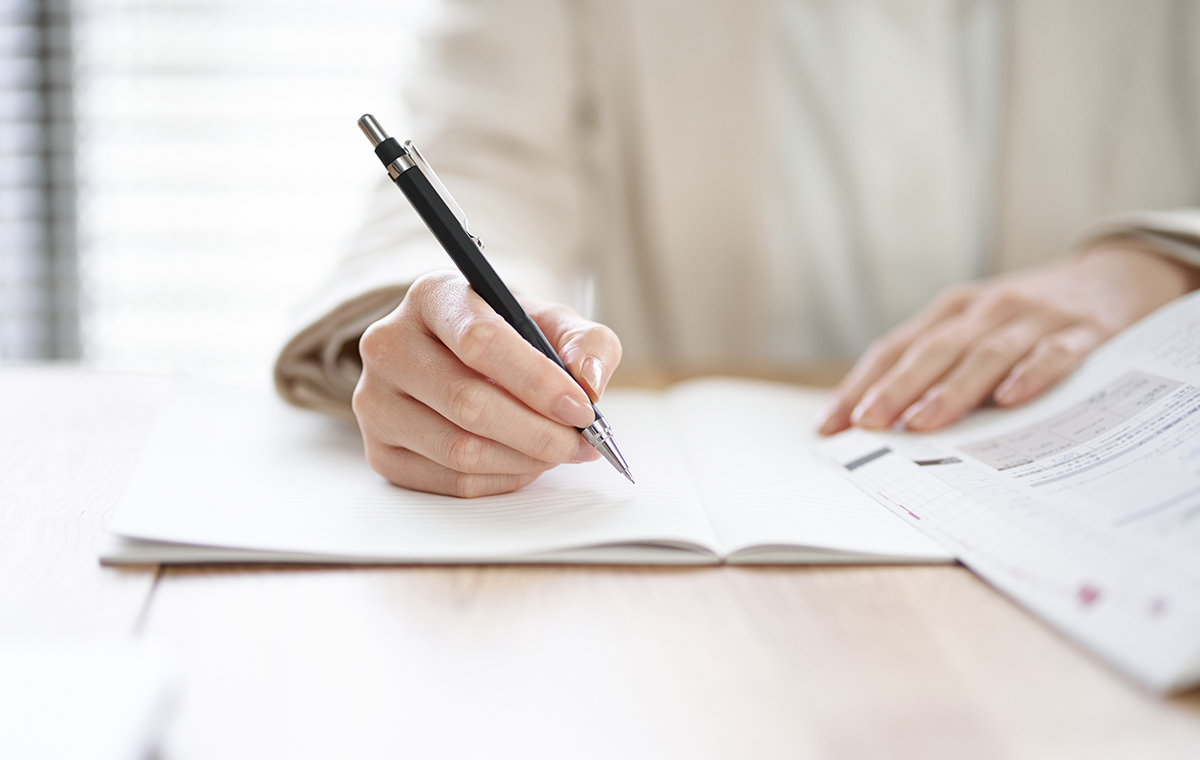 ペンでノートに何かを書いている人の手元の写真