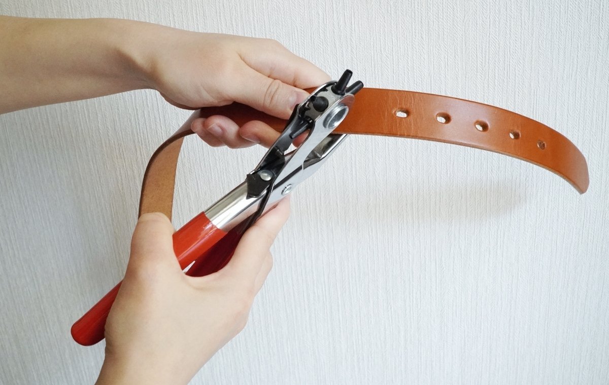 レザーパンチでベルトに穴を開けている写真