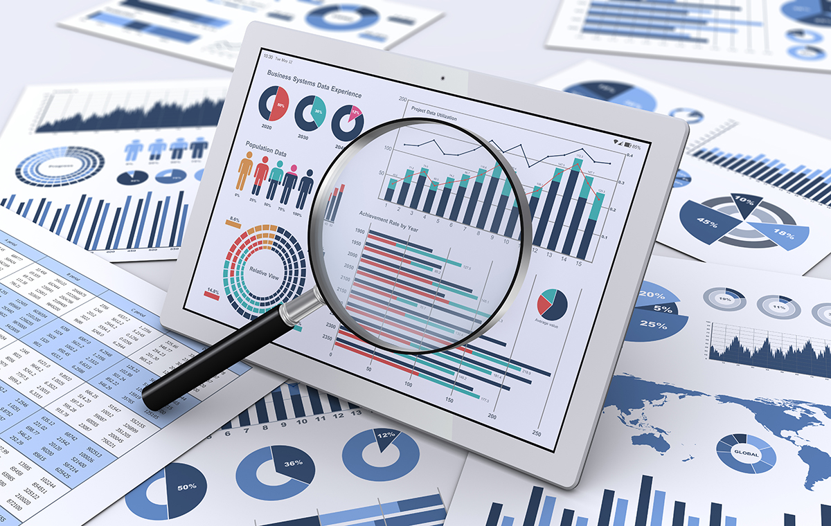 無造作に並べられた資料の上に、グラフが映し出されたタブレットと虫眼鏡が置いてあるイメージ画像