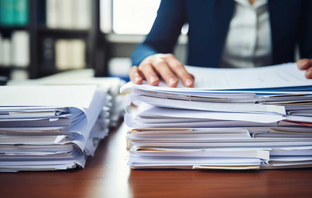 積み重ねられた資料の上に手を置いている人の写真
