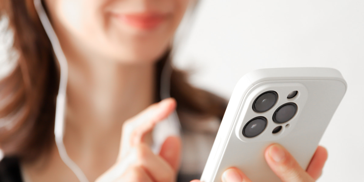 イヤホンをつけてスマホを操作しほほ笑む女性