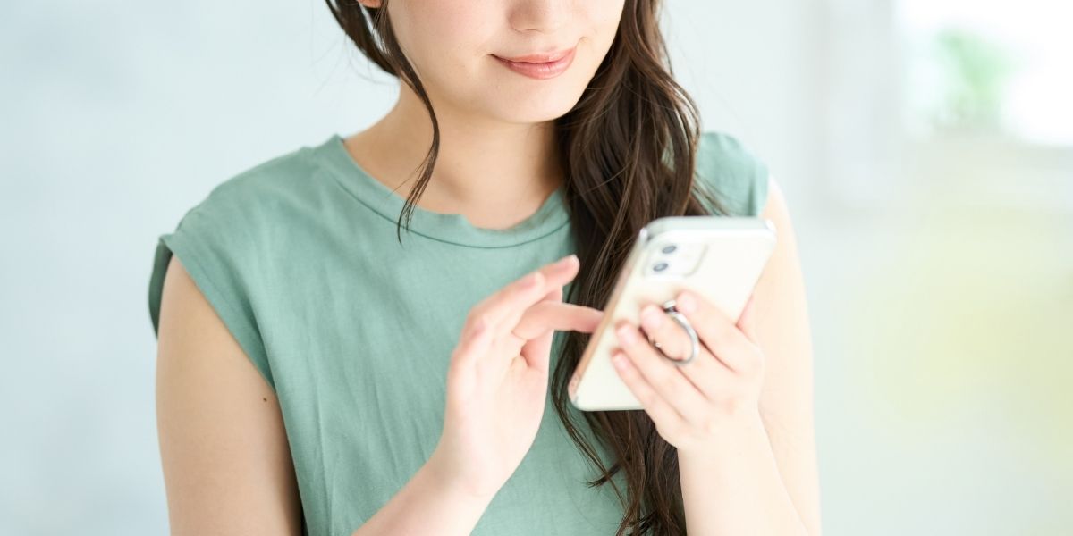 にこやかにスマホを操作する女性の写真