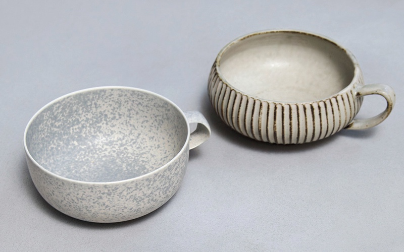 右／鎬スープカップ［小倉夏樹 灰粉引 ／直径（持ち手含む）15.5×高さ5.5cm］￥3,850（KOHORO）　左／スープカップ ［HIDAMARI nami/ 直径13.5（持ち手含む）×高さ5cm］￥4,180（VIVO.VA〈yumiko iihoshi porcelain〉）