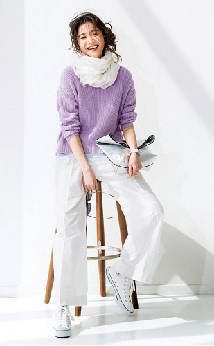 ラベンダー色ニットの裾からサックスブルーのTシャツを覗かせ、白パンツをあわせたモデル写真