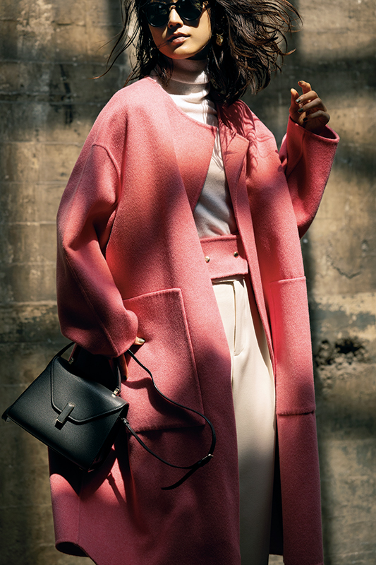 白っぽいニットとパンツにピンクのノーカラーのロングコートをはおったモデル写真