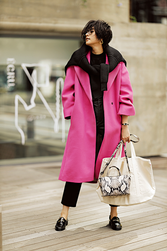 黒のニットとパンツにショッキングピンクのロングコートをはおり、その上から黒のニットを肩掛けして袖を結んだモデル写真