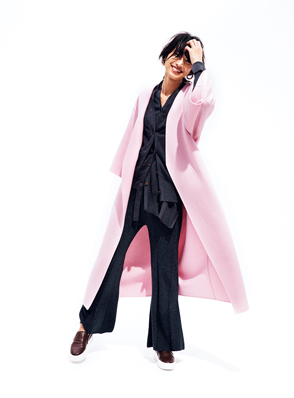 黒っぽいニットとパンツに薄いピンクのロング丈のノーカラーガウンコートをはおったモデル写真