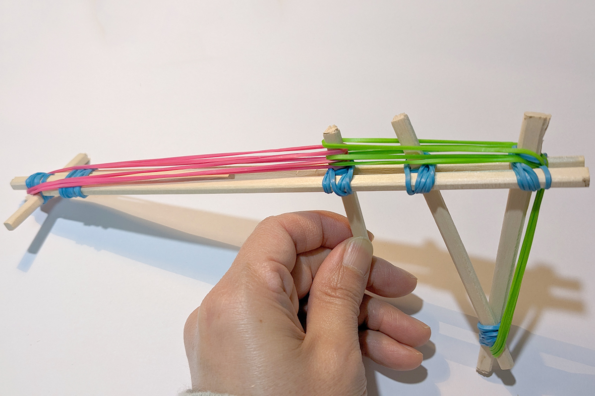 トリガーからグリップの上部を通ってグリップの下部分に緑の輪ゴム、先端からトリガーにかけて赤の輪ゴムがかかっている割り箸鉄砲の写真